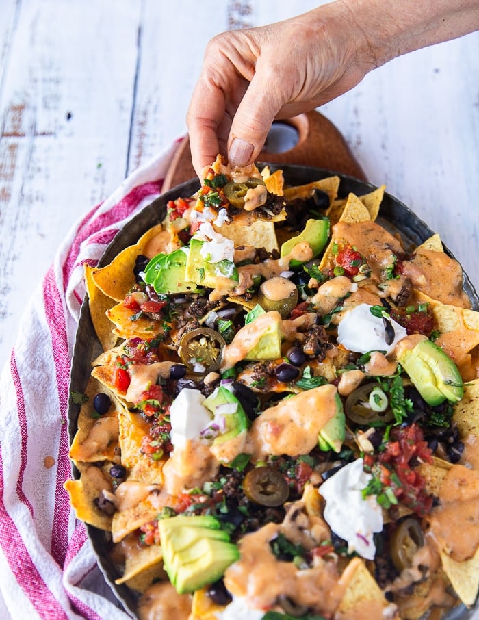 A hand pulling a nachos piece from the plate