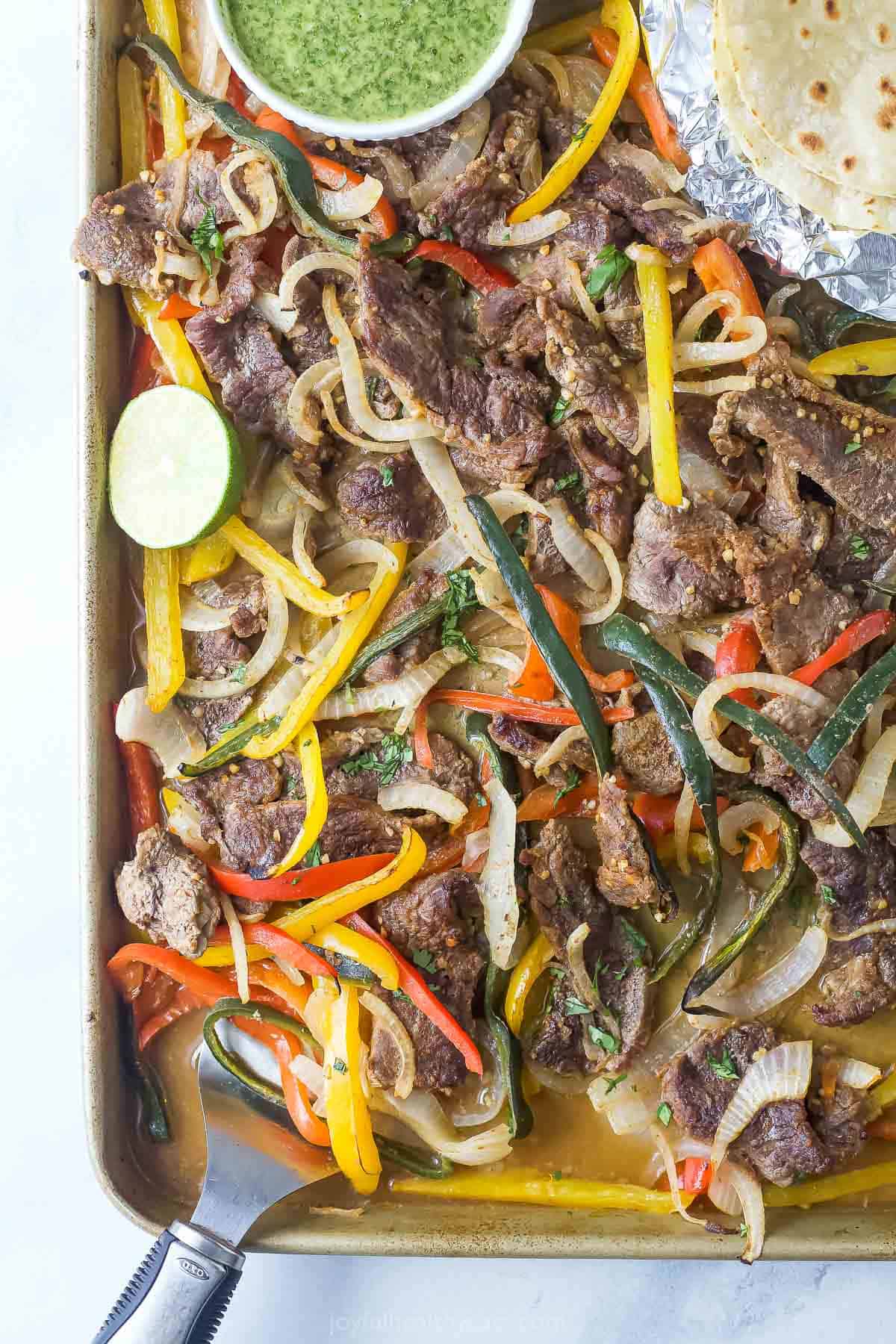 Homemade beef fajitas with bell peppers, poblanos, and onions in a baking sheet.