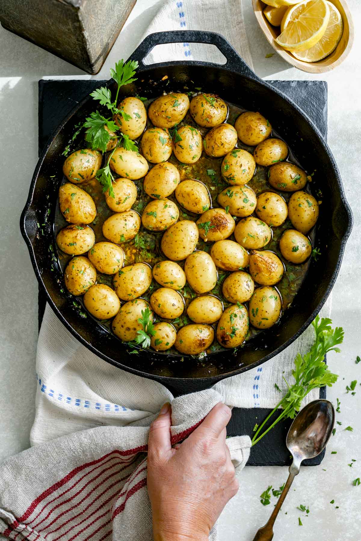 the Greek-Style Potatoes recipe in a cast iron skillet with parsley sprigs and lemon wedges